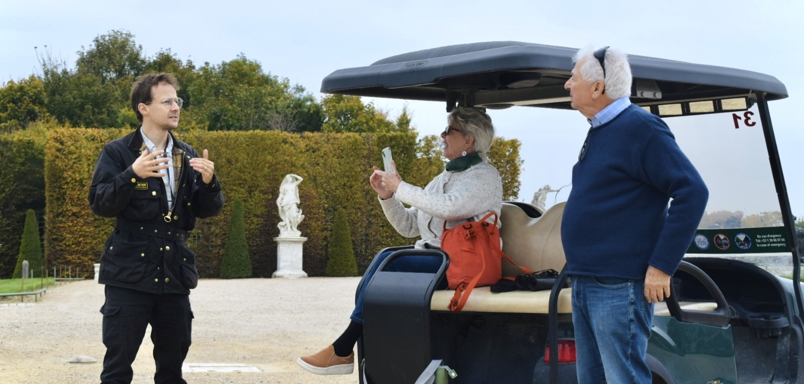 A family enjoying the golf carts of Versailles, with the maze of the royal gardens in the background